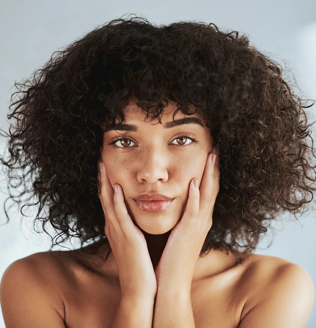 Woman with really curly full hair with her hands on her cheeks | Aviclear | NYC