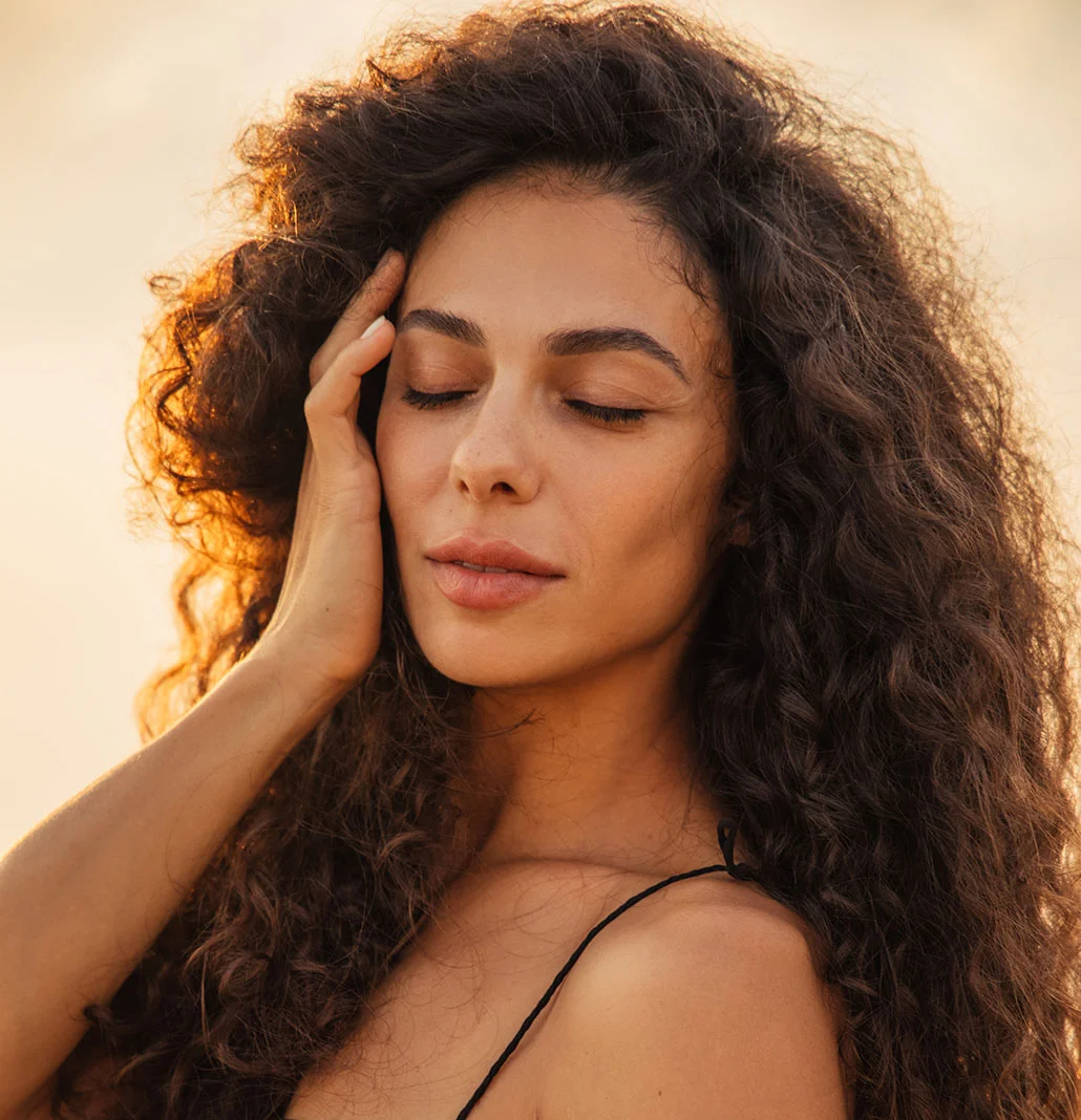 Middle aged woman with full, curly hair with her hand to her face and her eyes closed | BOTOX | NYC