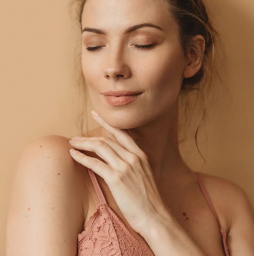 Woman wearing a salmon colored bra with her eyes closed and touching her neckline | Kybella | NYC