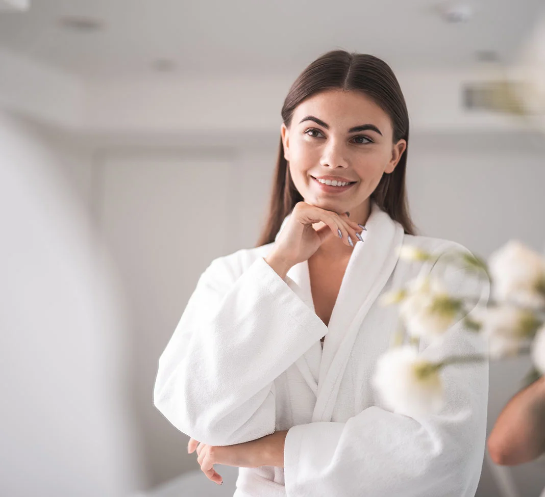 Woman in a white robe looking in the mirror | Kybella | NYC