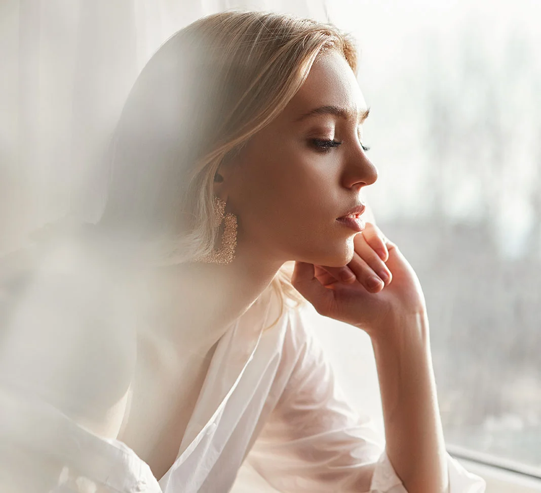 Side profile photo of a blonde haired woman looking out her window | Lip Fillers | NYC