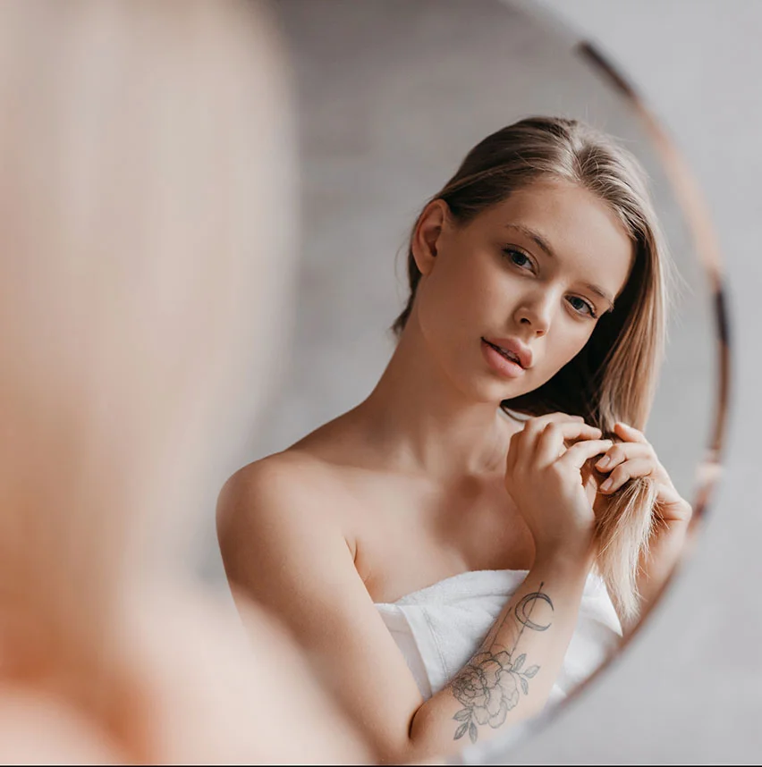 Youthful woman looking in the mirror and playing with her hair | Rhinoplasty | NYC