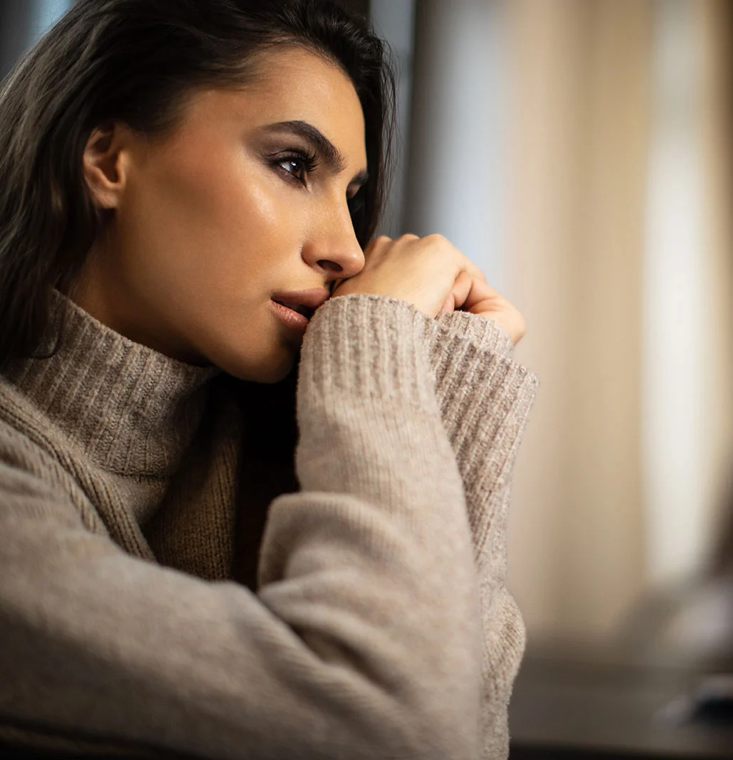 Brunette woman in a sweater looking to the side| Rhinoplasty | NYC
